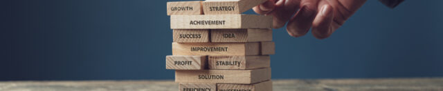 Wide view image of businessman stacking wooden pegs with words of business development and success written on them. Over blue background.