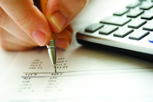 Person calculating finances using a calculator and pen on a paper document.